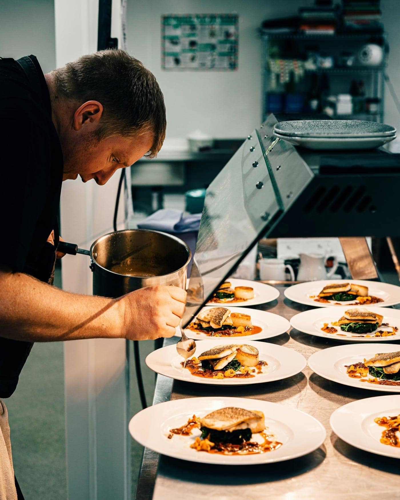 Chefs plating dishes under the warm copper lamps of a restaurant pass